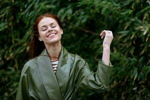 mulher com uma lindo sorrir posando contra a verde bambu dentro primavera, vermelho vôo cabelo dentro a ventoso clima, a conceito do estilo e moda foto