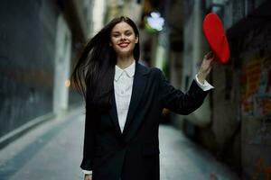 moda mulher sorrir com dentes e Diversão turista dentro à moda roupas dentro Jaqueta e vermelho boina caminhando baixa limitar cidade rua vôo cabelo, viagem, francês estilo, cinematográfico cor, retro vintage estilo. foto