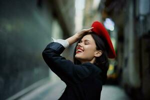 moda mulher sorrir com dentes e Diversão turista dentro à moda roupas dentro Jaqueta e vermelho boina caminhando baixa limitar cidade rua vôo cabelo, viagem, francês estilo, cinematográfico cor, retro vintage estilo. foto