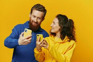 homem e mulher casal sorridente alegremente com telefone dentro mão social meios de comunicação vendo fotos e vídeos, em amarelo fundo, símbolos sinais e mão gestos, família freelancers.