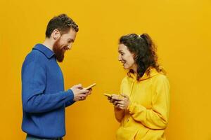 mulher homem alegre casal com telefones dentro mão social trabalho em rede e comunicação torto sorrir Diversão e lutar, dentro amarelo fundo. a conceito do real família relacionamentos, freelancers, trabalhos on-line. foto