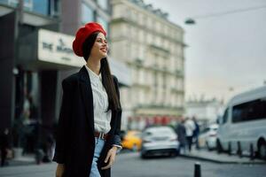 uma sorrir mulher com o negócio dentes anda em dentro a cidade contra a pano de fundo do escritório edifícios, à moda elegante roupas e inventar, Primavera andar, viagem. foto