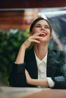 à moda mulher senta dentro uma cafeteria às uma mesa e fuma uma cigarro liberando fumaça a partir de dela boca, uma mau hábito, uma sorrir com dentes e uma pensativo Veja foto