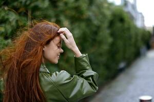 mulher com uma lindo sorrir posando contra uma verde bambu dentro primavera, vermelho vôo cabelo dentro a ventoso clima, a conceito do estilo e moda dentro a cidade foto