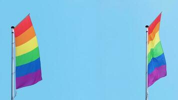 dois vertical arco Iris ou lgbtq orgulho bandeiras mosca em mastro de bandeira contra azul céu com cópia de espaço foto