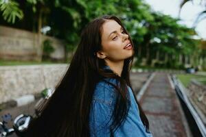 retrato do uma mulher morena sorrir com dentes caminhando lado de fora contra uma pano de fundo do Palma árvores dentro a trópicos, verão Férias e ao ar livre lazer, a despreocupado estilo de vida do uma freelance estudante. foto