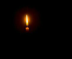 uma única chama de vela acesa ou luz brilhando em uma vela laranja em fundo preto ou escuro na mesa na igreja para o natal, funeral ou serviço memorial com espaço de cópia foto