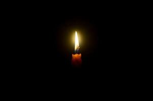 uma solteiro queimando vela chama ou luz brilhando espiral laranja vela em Preto ou Sombrio fundo em mesa dentro Igreja para Natal, velório ou memorial serviço com cópia de espaço foto