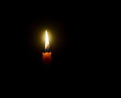 uma solteiro queimando vela chama ou luz brilhando em espiral laranja vela em Preto ou Sombrio fundo em mesa dentro Igreja para Natal, velório ou memorial serviço com cópia de espaço foto