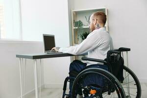 uma homem cadeira de rodas homem de negocios com tatuagens dentro a escritório trabalho às uma computador portátil on-line, o negócio processo, uma cadeira de rodas fechar-se, integração para dentro sociedade, a conceito do trabalhando uma pessoa com deficiências foto