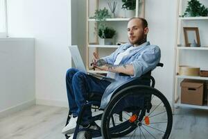 homem dentro cadeira de rodas trabalhador autonomo trabalhando às computador portátil às casa sorriso, trabalhando on-line, social redes e comece, cópia de espaço, social integração, saúde conceito homem com deficiências, real pessoa foto