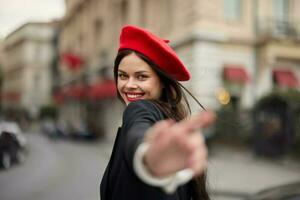 moda mulher sorrir com dentes em pé em a rua dentro frente do a cidade turista Segue mim à moda roupas com vermelho lábios e vermelho boina, viagem, cinematográfico cor, retro vintage estilo, urbano moda. foto