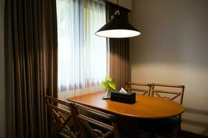 Sombrio casa interior com madeira jantar mesa aceso de lâmpada, tarde luz para jantar. foto