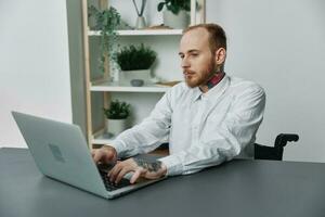 uma homem dentro uma cadeira de rodas uma homem de negocios com tatuagens dentro a escritório trabalho às uma computador portátil, integração para dentro sociedade, a conceito do trabalhando uma pessoa com deficiências, liberdade a partir de social frameworks foto