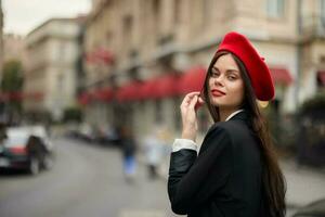 moda mulher retrato sorrir dentes em pé em a rua dentro a cidade fundo dentro à moda roupas com vermelho lábios e vermelho boina, viagem, cinematográfico cor, retro vintage estilo, urbano moda estilo de vida. foto