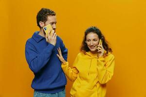 mulher e homem alegre casal com telefones dentro mão falando em célula telefone torto sorrir alegre, em amarelo fundo. a conceito do real família relacionamentos, falando em a telefone, trabalhos on-line. foto