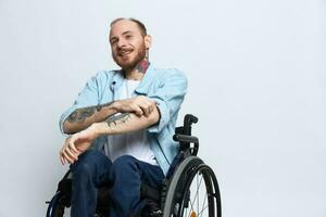uma homem dentro uma cadeira de rodas sorriso, cópia de espaço, com tatuagens em dele braços senta em uma cinzento estúdio fundo, a conceito do saúde é uma pessoa com deficiências, uma real pessoa foto