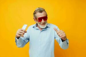 velho homem dentro elegante vermelho óculos com uma telefone amarelo fundo foto