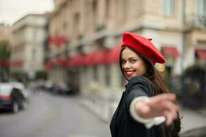 moda mulher sorrir com dentes em pé em a rua dentro frente do a cidade turista Segue mim à moda roupas com vermelho lábios e vermelho boina, viagem, cinematográfico cor, retro vintage estilo, urbano moda. foto