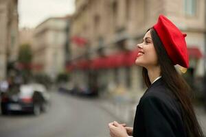 moda mulher sorrir com dentes em pé em a rua dentro frente do a cidade turista dentro à moda roupas com vermelho lábios e vermelho boina, viagem, cinematográfico cor, retro vintage estilo, urbano moda. foto