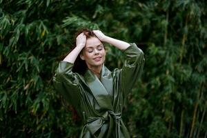 mulher com uma lindo sorrir posando contra a verde bambu dentro primavera, vermelho vôo cabelo dentro a ventoso clima, a conceito do estilo e moda foto