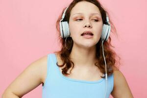 retrato do uma jovem menina dentro fones de ouvido ouvindo para música em uma Rosa fundo inalterado foto