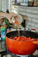 chefe de cozinha derrama a Osso Buco molho dentro uma panela sobre baixo calor foto