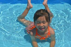 feliz pequeno menina natação piscina em uma quente verão dia. crianças aprender para nadar. criança água brinquedos. crianças jogar dentro tropical resorts. família de praia período de férias. foto