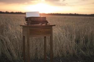 máquina de escrever em uma mesa de cabeceira de nogueira em um campo de trigo ao pôr do sol foto