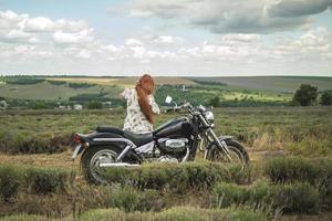 garota ruiva em um vestido branco e botas junto com um campo de lavanda de motocicleta foto