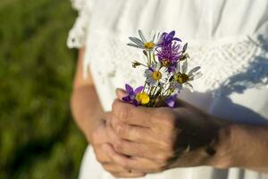 mulher dentro uma branco vestir detém uma ramalhete do flores silvestres dentro dela mãos foto