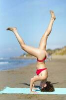 fino mulher praticando ioga em arenoso de praia foto