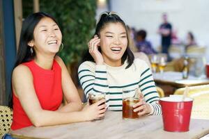 alegre ásia mulheres em repouso dentro cafeteria com bebidas foto