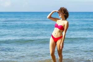 fino mulher dentro bikini em pé dentro água do mar foto