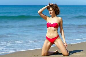 fino mulher dentro bikini em pé em arenoso de praia foto