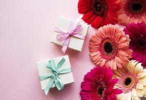 flores gerbera e caixas de presente em um fundo rosa foto