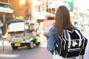 viajante viagem em período de férias fim de semana, feriado dentro verão, sorrir bonita ásia jovem viajando mulher mochileiro a partir de atrás ou voltar, caminhando dentro khao san estrada, rua ao ar livre mercado, vida cidade dentro Bangkok. foto