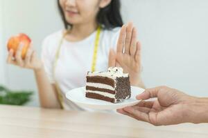 dieta, dieta pouco saudável ásia jovem mulher mão dentro empurrar fora, rejeitando comer chocolate bolo ou doce gosto, brigando para manter isto a partir de obtendo gordo quando pessoa trazer para meu. saudável, nutrição do peso perda foto