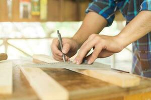 carpintaria profissional, mão do ásia jovem homem, masculino carpinteiro usar fita medir, ferramenta em borda madeira dentro pequeno fazer compras. carpintaria, mobília fazendo, construção indústria. proprietário pequeno o negócio pessoas. foto