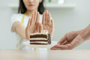 dieta, dieta pouco saudável ásia jovem mulher mão dentro empurrar fora, rejeitando comer chocolate bolo ou doce gosto, brigando para manter isto a partir de obtendo gordo quando pessoa trazer para meu. saudável, nutrição do peso perda foto