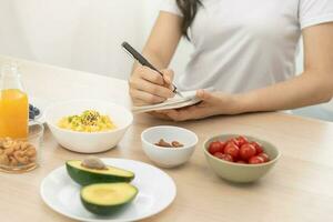 dieta, dieta mão do ásia jovem mulher, menina escrever dieta plano nutrição em mesa é diferente Comida ingredientes dentro a verde. nutricionista do saudável, nutrição do peso perda, saúde Cuidado pessoas. foto