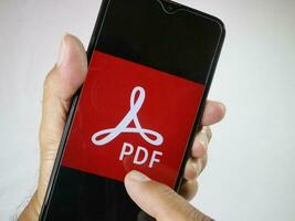 Jacarta, Indonésia, 2023. mão segurando Móvel telefone com dedo toque a pdf logotipo em tela. foto