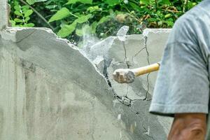 mão do trabalhador usando martelo esmagador e demolir em tijolo parede às construção local foto