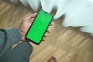 jovem homem mão usando inteligente telefone com verde tela às casa foto