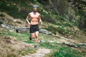 uma desportivo homem com músculos corre em uma montanha trilha foto