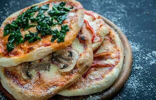 mini pizzas com várias coberturas na placa de madeira foto