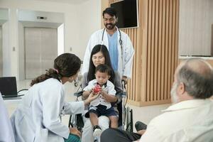 feliz jovem fêmea pediatra médico dentro uniforme provocando pequeno Garoto dentro cadeira de rodas para médico exame às ambulatório clínica hospital, pessoas público saúde Cuidado checar, e compromisso Visita. foto