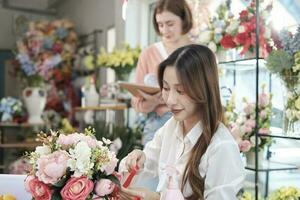 dois jovem lindo fêmea florista parceiros trabalhando com grupo do flores arranjo, decoração com adorável ornamentado, compra ordem trabalhos dentro colorida flor fazer compras loja, sme o negócio empreendedor. foto