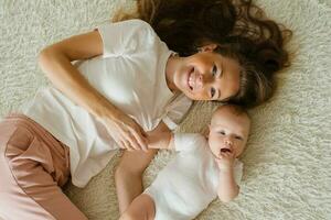 caucasiano mãe mentiras em a cama com dela bebê filho e sorrisos Felizmente. topo Visão do a família foto