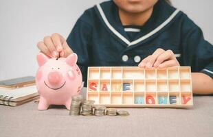 pequeno menina colocando moeda para dentro porquinho banco para salvando com pilha do moedas em mesa foto